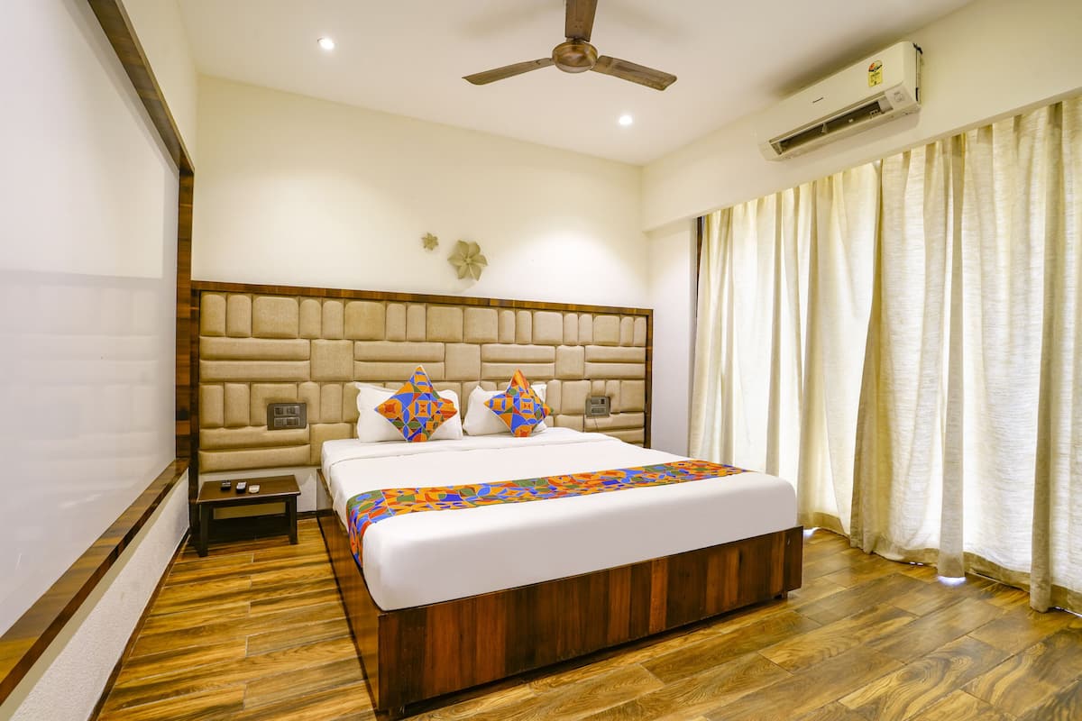 A bedroom with a large bed, wooden floor, a ceiling fan, an air conditioning unit, and a nightstand.