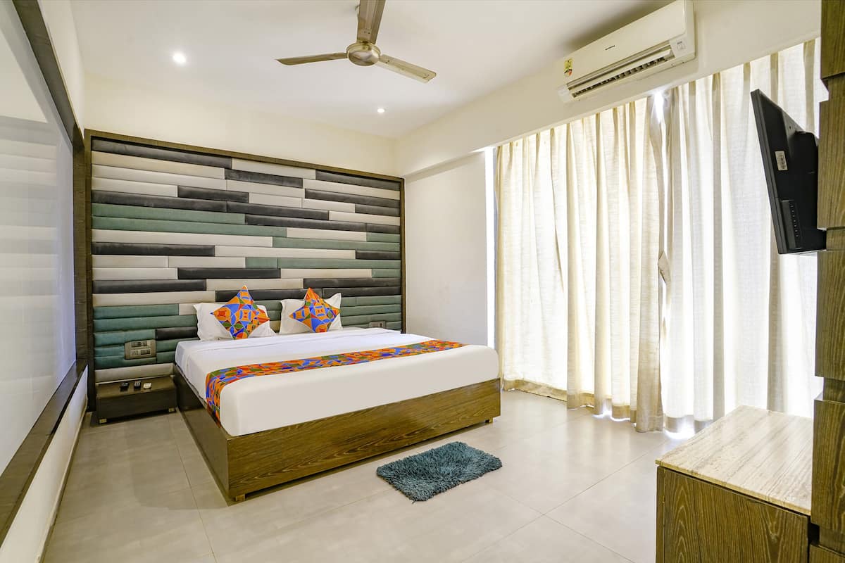 A modern hotel room with a large bed, a ceiling fan, an air conditioning unit, and a TV mounted on the wall.