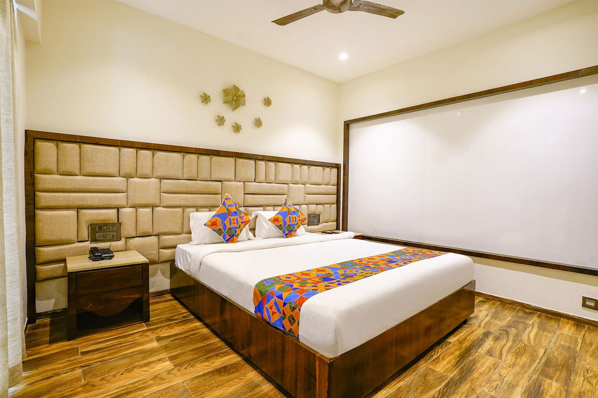 A hotel room with a large bed, wooden headboard, a nightstand with a phone, and a ceiling fan.