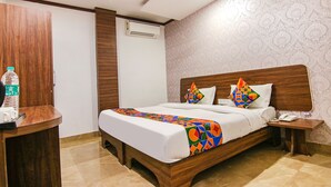 A hotel room with a wooden bed, a nightstand, a bedside table, a ceiling fan, an air conditioning unit, and a patterned wall. - Fabexpress The Divine Residency (New Delhi)