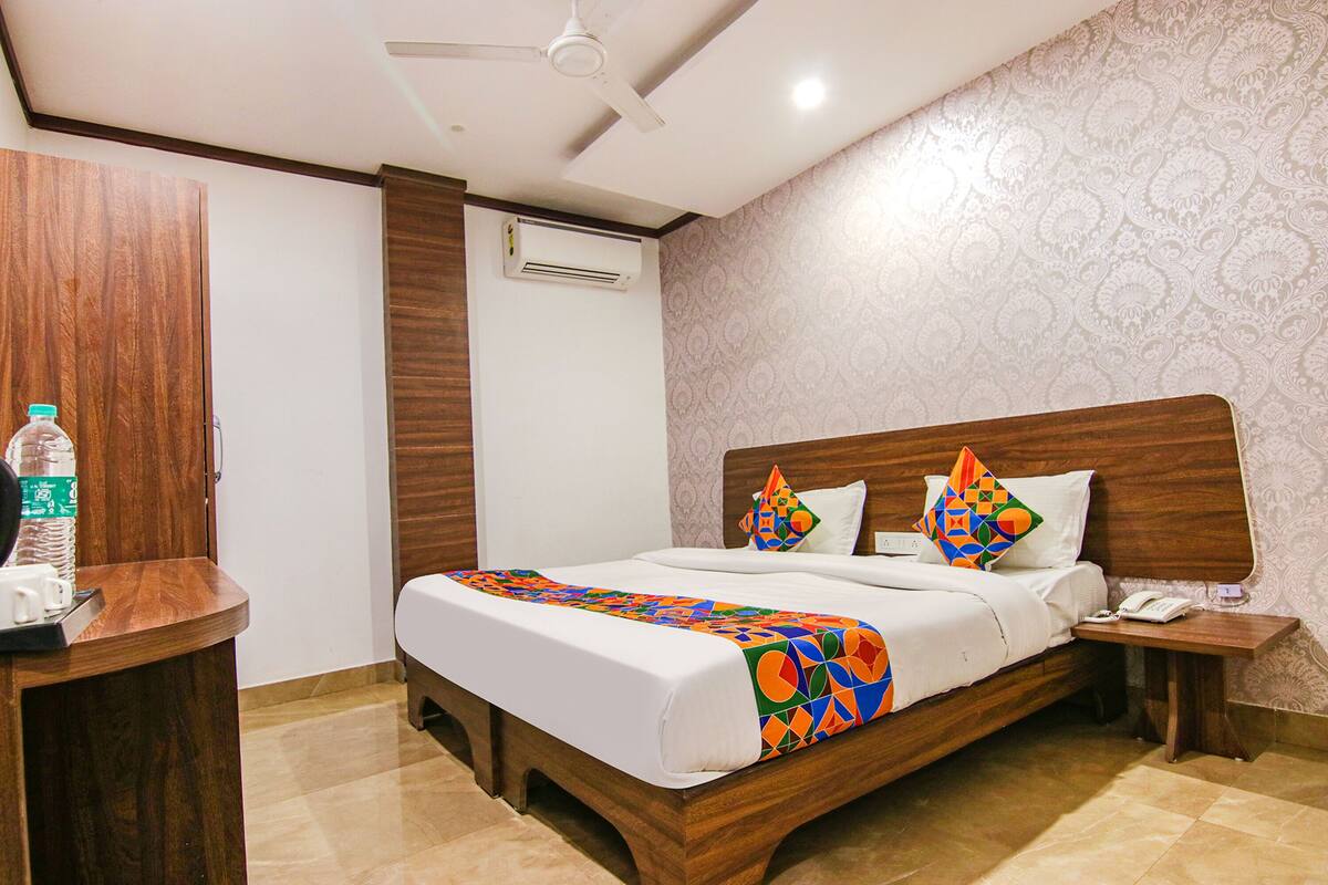 A hotel room with a wooden bed, a nightstand, a bedside table, a ceiling fan, an air conditioning unit, and a patterned wall.