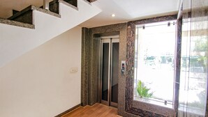 A modern elevator with a digital display, a marble wall, and a wooden floor. - Fabexpress The Divine Residency (New Delhi)