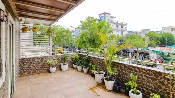 A balcony with potted plants, a stone wall, and a view of a commercial area with shops and people. - Fabexpress The Divine Residency (New Delhi)