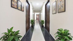 A hotel hallway with a polished floor, framed floral artwork on the walls, and potted plants at the ends. - Fabexpress Golden Wings (Udaipur)