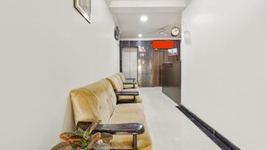 A hotel lobby with a reception desk, a clock, a television, and a seating area with a plant. - Fabexpress Golden Wings (Udaipur)