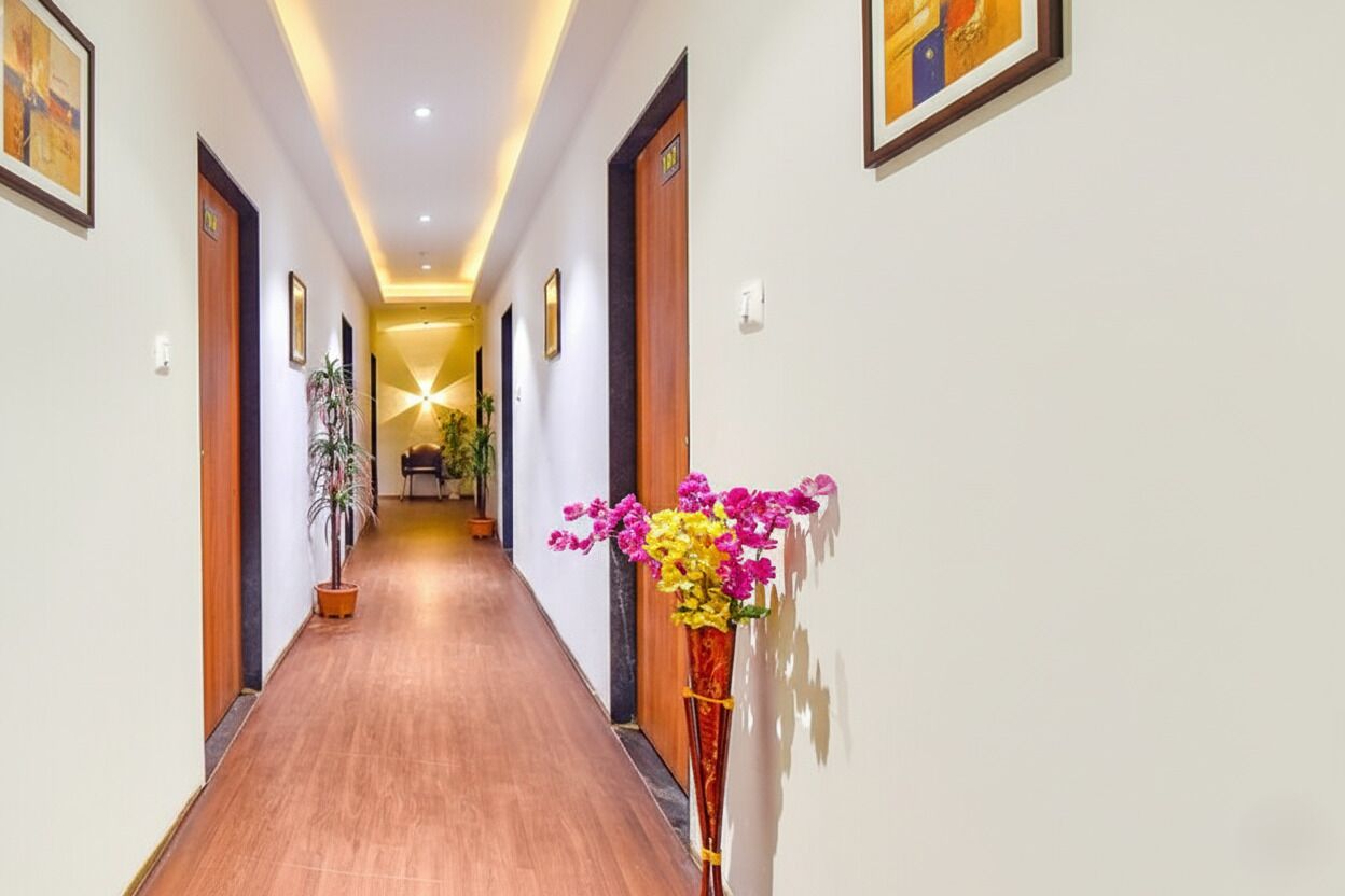 A hotel hallway with wooden flooring, framed artwork on the walls, and a vase of flowers on the right.