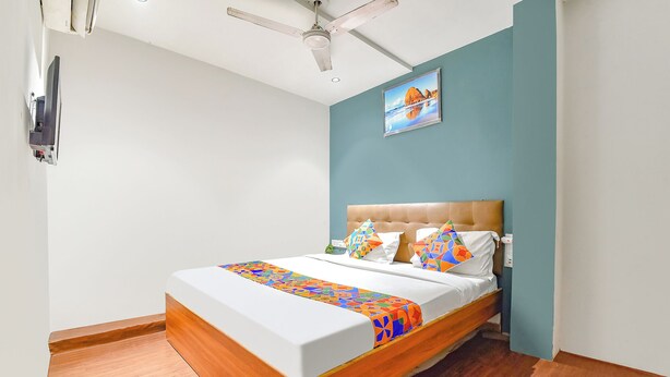 A bedroom with a bed, a ceiling fan, a wall-mounted TV, and a framed picture. - Fabhotel Nidhivan (Surat)