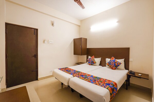 A hotel room with two beds, a desk, a phone, and a door.