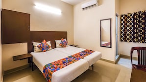A hotel room with a double bed, a nightstand, a desk, an air conditioning unit, a mirror, and a patterned curtain. - Fabexpress Joel Inn (Chennai)