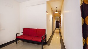 A hallway with a red sofa, white walls, and a patterned curtain. - Fabexpress Joel Inn (Chennai)