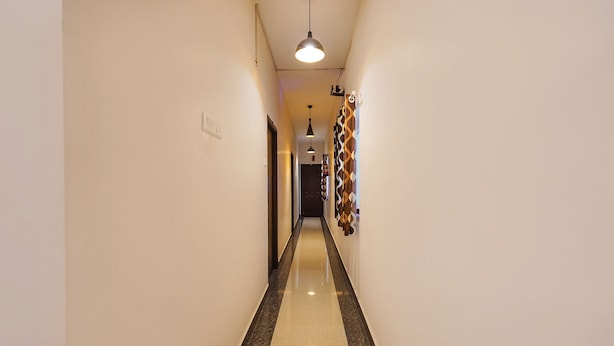A narrow hallway with a polished floor, a hanging pendant light, and a patterned wall decoration. - Fabexpress Joel Inn (Chennai)