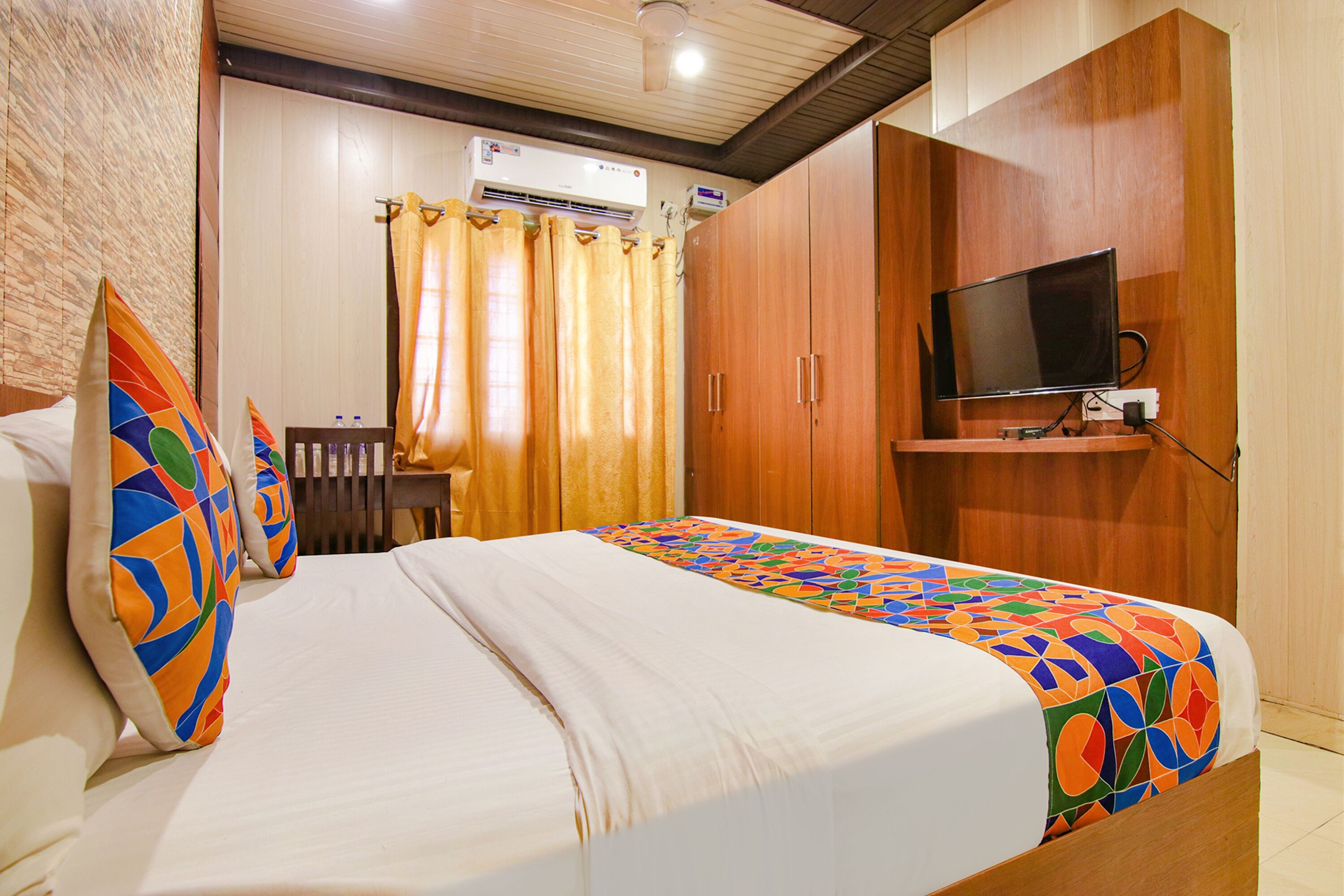A hotel room with a bed, a TV mounted on the wall, and a window with curtains.