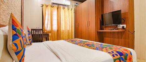 A hotel room with a bed, a TV mounted on the wall, and a window with curtains.