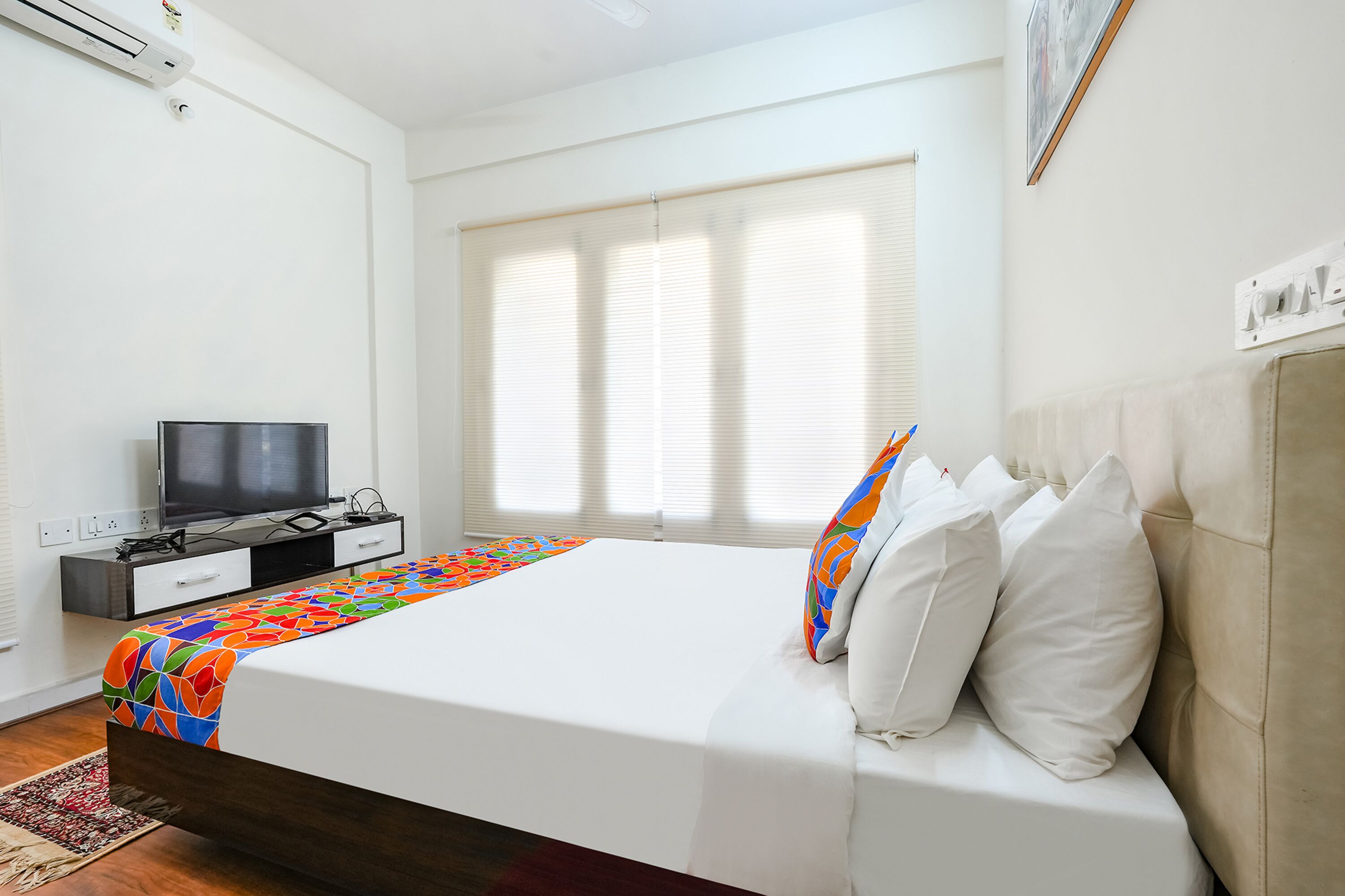 Une chambre d’hôtel moderne équipée d’un lit, d’une télévision et d’une fenêtre avec des stores.