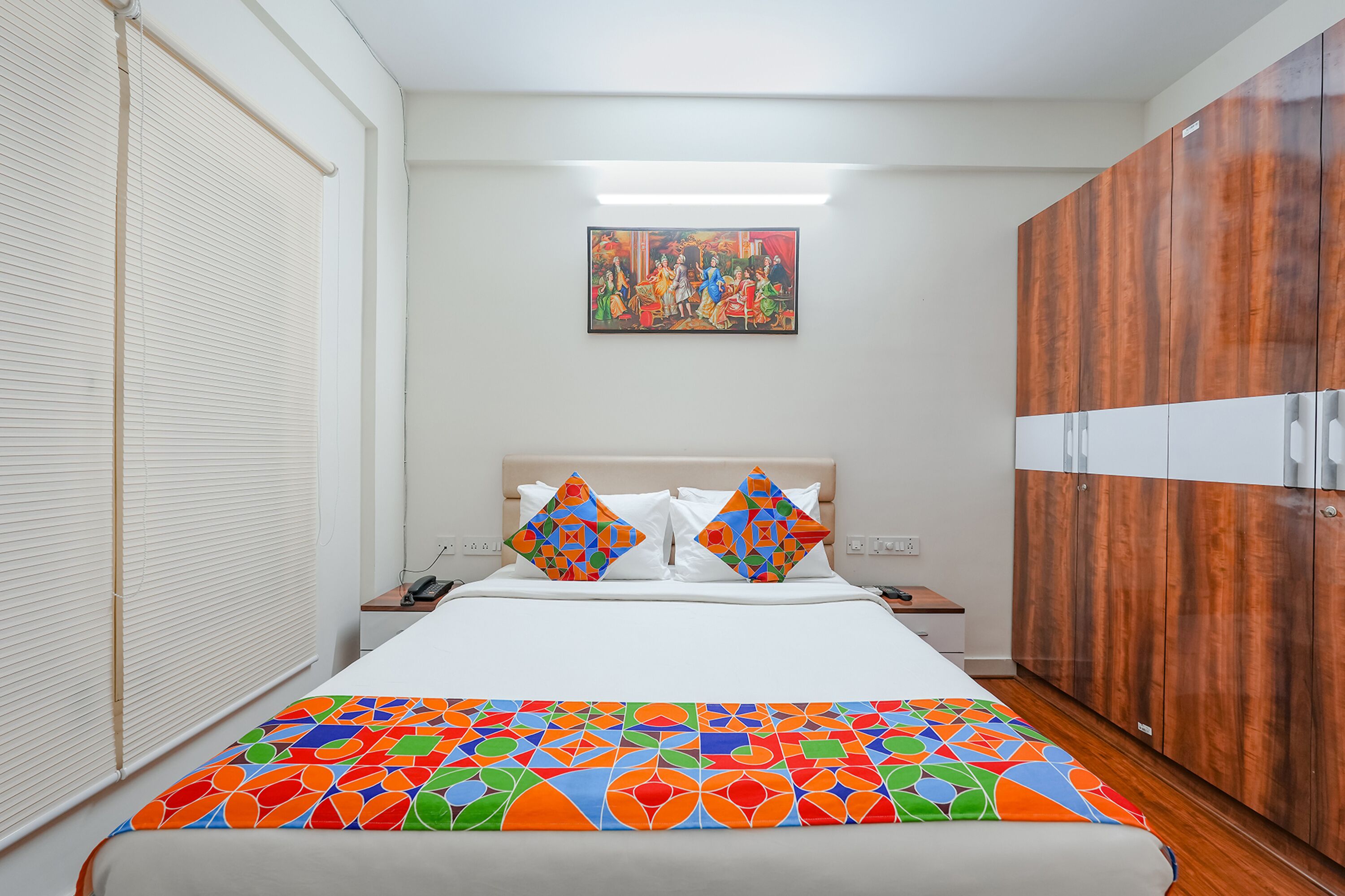 A hotel room with a bed, a nightstand, a wardrobe, and a painting on the wall.