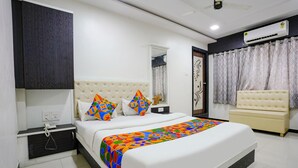 A modern bedroom with a large bed, a bedside table, a nightstand, a chair, and an air conditioning unit. - Fabexpress Rajmahal (Navi Mumbai)