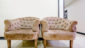 Two tufted armchairs with wooden legs and a patterned fabric, positioned in a hallway with a tiled floor and a white wall. - Fabexpress Rajmahal (Navi Mumbai)
