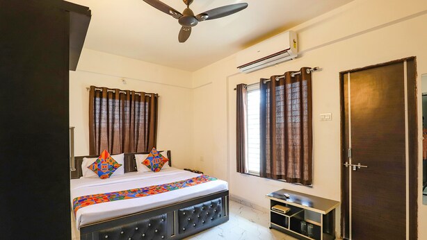 A bedroom with a bed, a ceiling fan, an air conditioning unit, a wardrobe, and a small table. - Fabhotel Elite Palm (Nagpur)