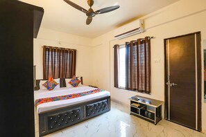 A bedroom with a bed, a ceiling fan, an air conditioning unit, a wardrobe, and a small table. - Fabhotel Elite Palm (Nagpur)