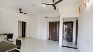 A spacious room with white walls, a marble floor, a table with chairs, and two ceiling fans. - Fabhotel Elite Palm (Nagpur)
