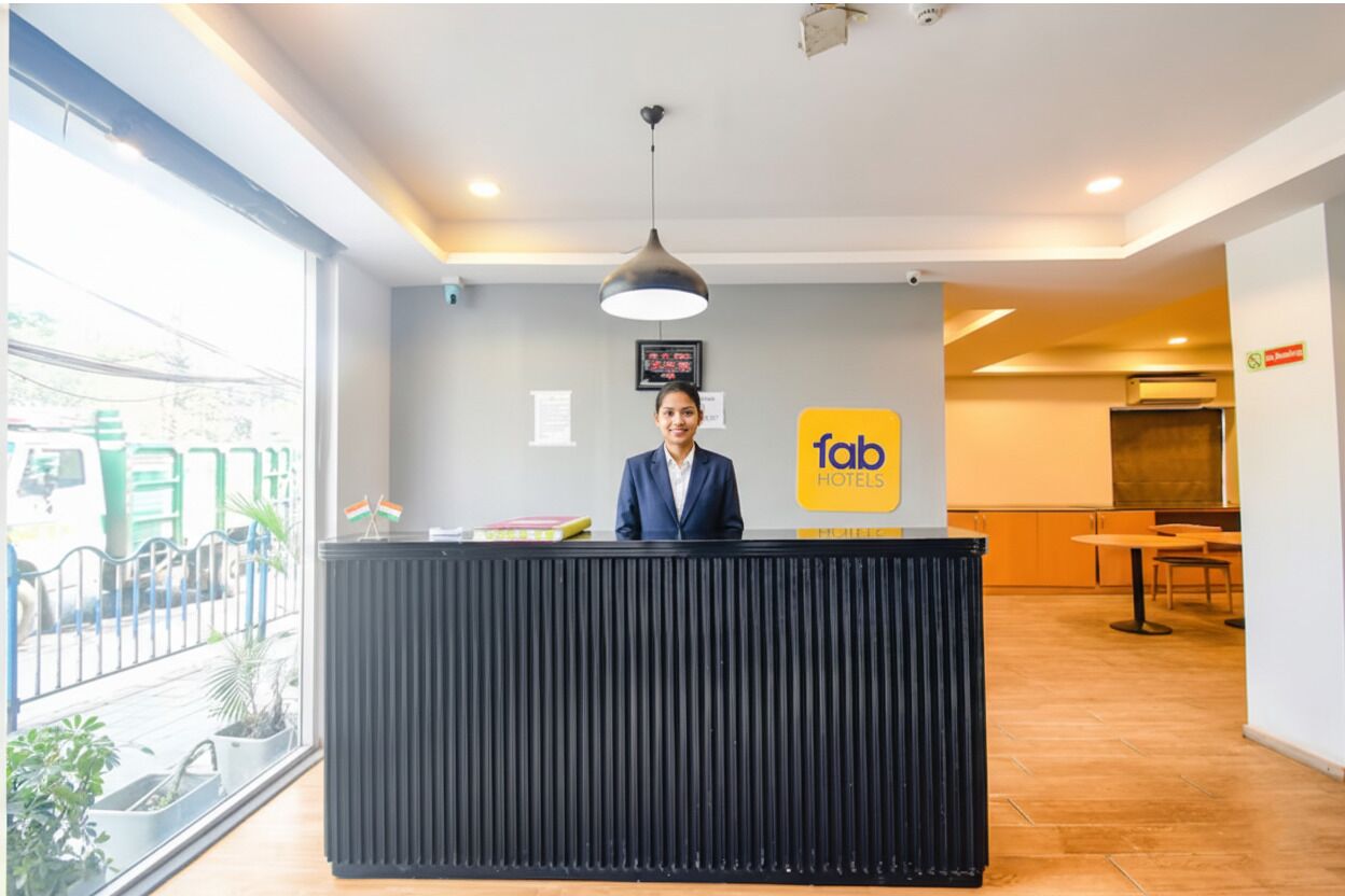 A hotel reception desk with a modern design, a visible sign for 'fab Hotels', and a view of the outside through large windows.