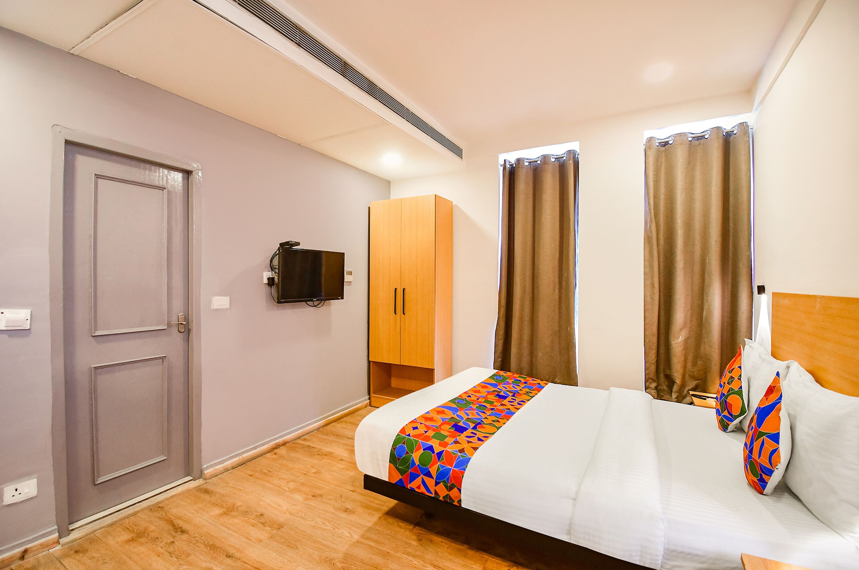 A hotel room with a bed, a wardrobe, a television, and curtains.