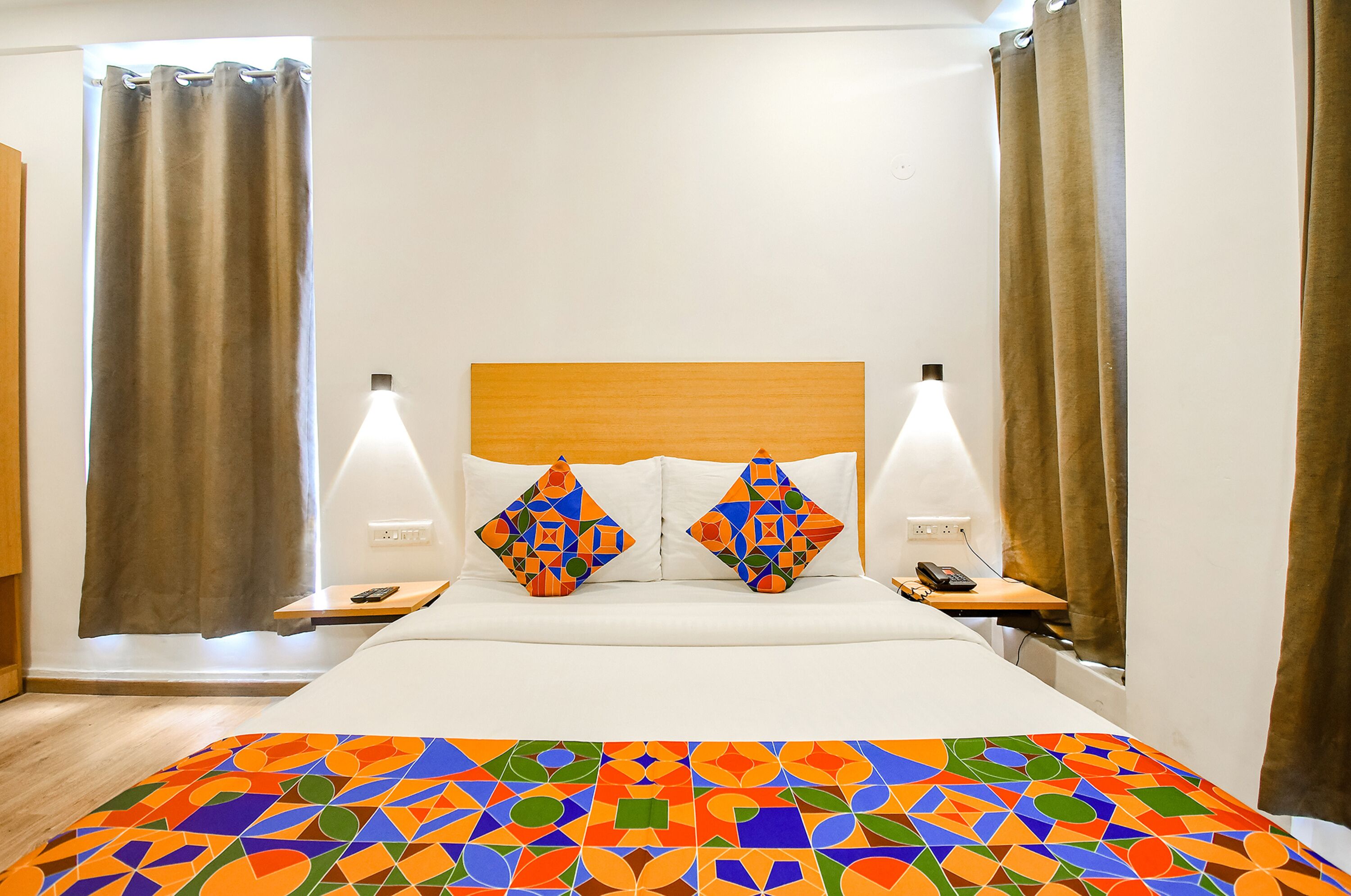 Une chambre d’hôtel avec un lit, deux oreillers, une table de chevet, une lampe et des rideaux.
