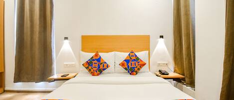 Une chambre d’hôtel avec un lit, deux oreillers, une table de chevet, une lampe et des rideaux.