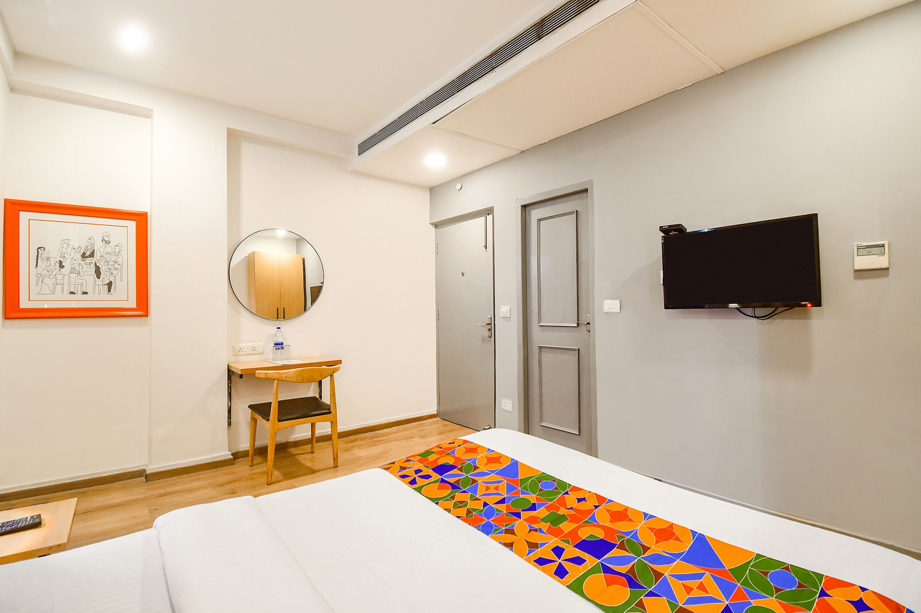 A hotel room with a bed, a desk, a chair, a mirror, a TV, and a door.
