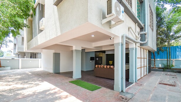 A covered outdoor area with a reception desk, a green mat, and a building with a light-colored facade and visible pipes. - Fabhotel Skylight Studio Rooms (Pune)