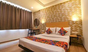 A hotel room with a bed, a desk, a chair, a mirror, and a wall with a patterned design. - Fabexpress La Serene (New Delhi)