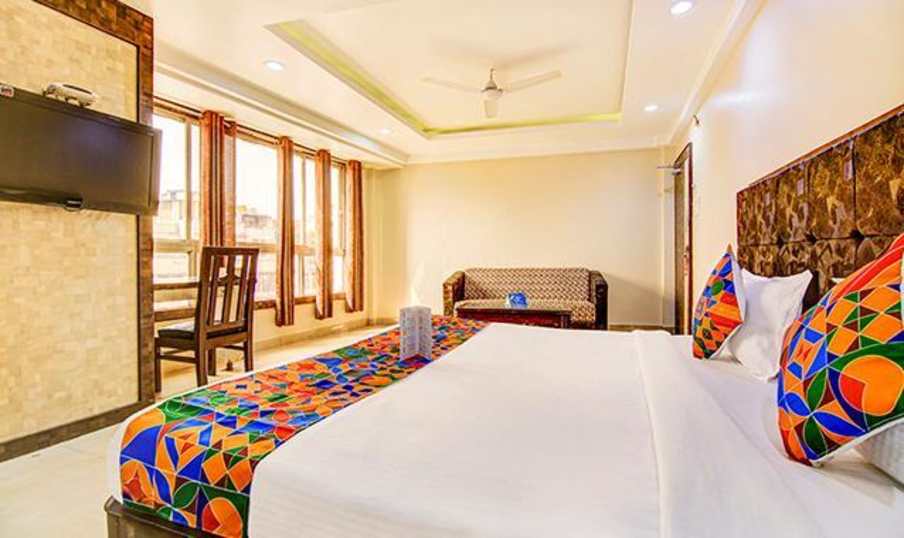 Quarto de hotel com uma cama grande, televisão na parede, um sofá e uma cadeira.