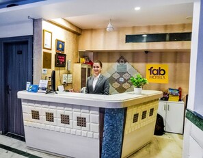 Hotellin vastaanottotiski, jossa on digitaalinen näyttö, kasvi ja kyltti, jossa lukee ”Fab Hotels”.