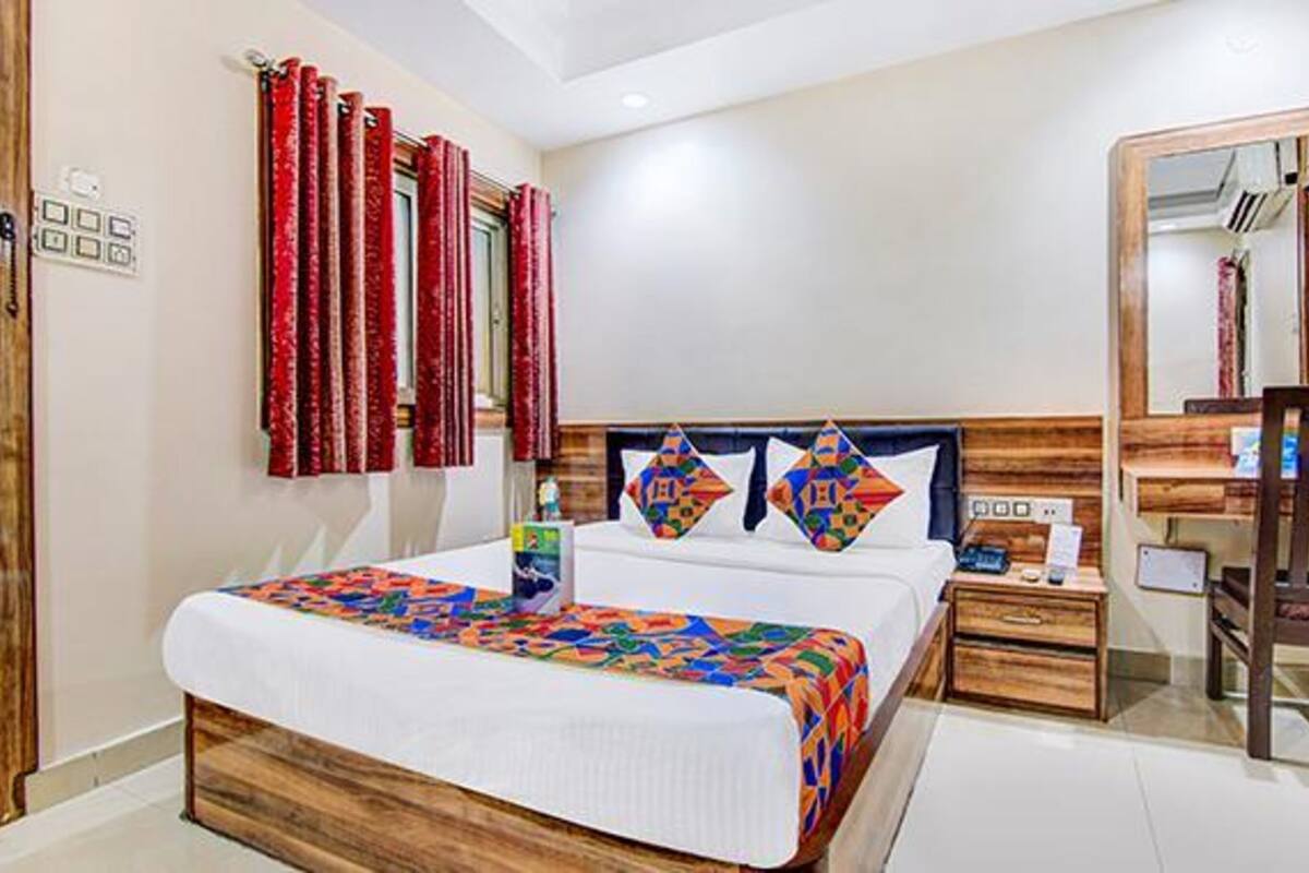Una camera d'albergo con un grande letto, una testiera in legno, un comodino, uno specchio e tende rosse.