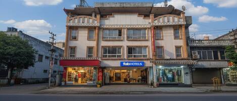 A multi-story building with a 'fabHOTELS' sign, storefronts on the ground floor, and a clear sky.