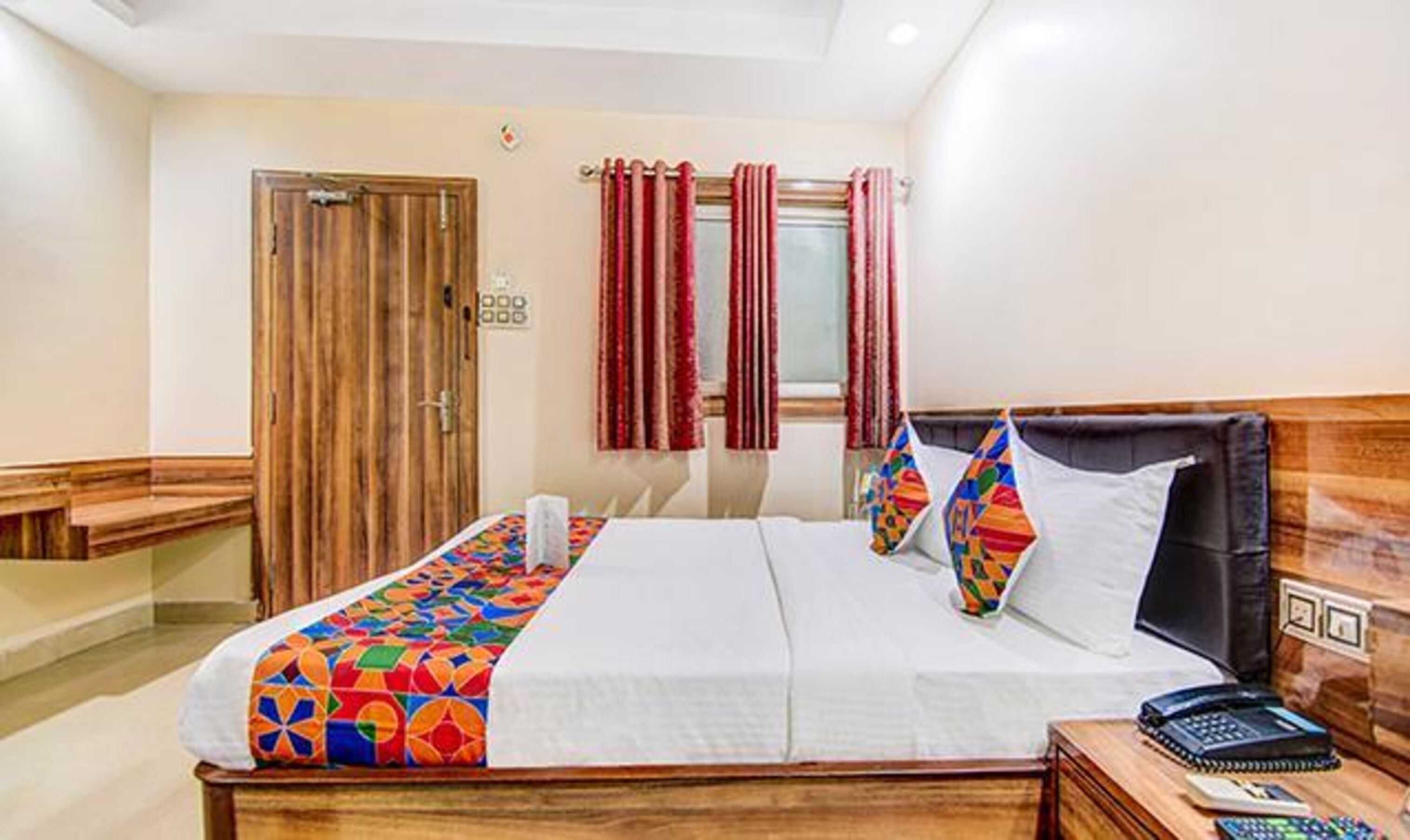 A hotel room with a wooden bed, a desk with a telephone, and a window with curtains.