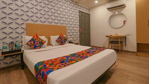 Ein Hotelzimmer mit einem großen Bett, einem Nachttisch mit Lampe, einem kleinen Schreibtisch mit Stuhl, einer Klimaanlage und einem Spiegel an der Wand.