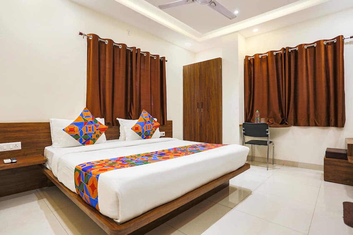 Une chambre d’hôtel avec un grand lit, une tête de lit en bois, deux oreillers, une couverture colorée, une chaise, un bureau et une armoire.