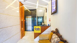 Zona de recepción de un hotel con suelo de mármol, mostrador de recepción y un sofá con cojín estampado.