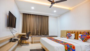 Una habitación de hotel con cama, escritorio, silla y televisión en la pared.