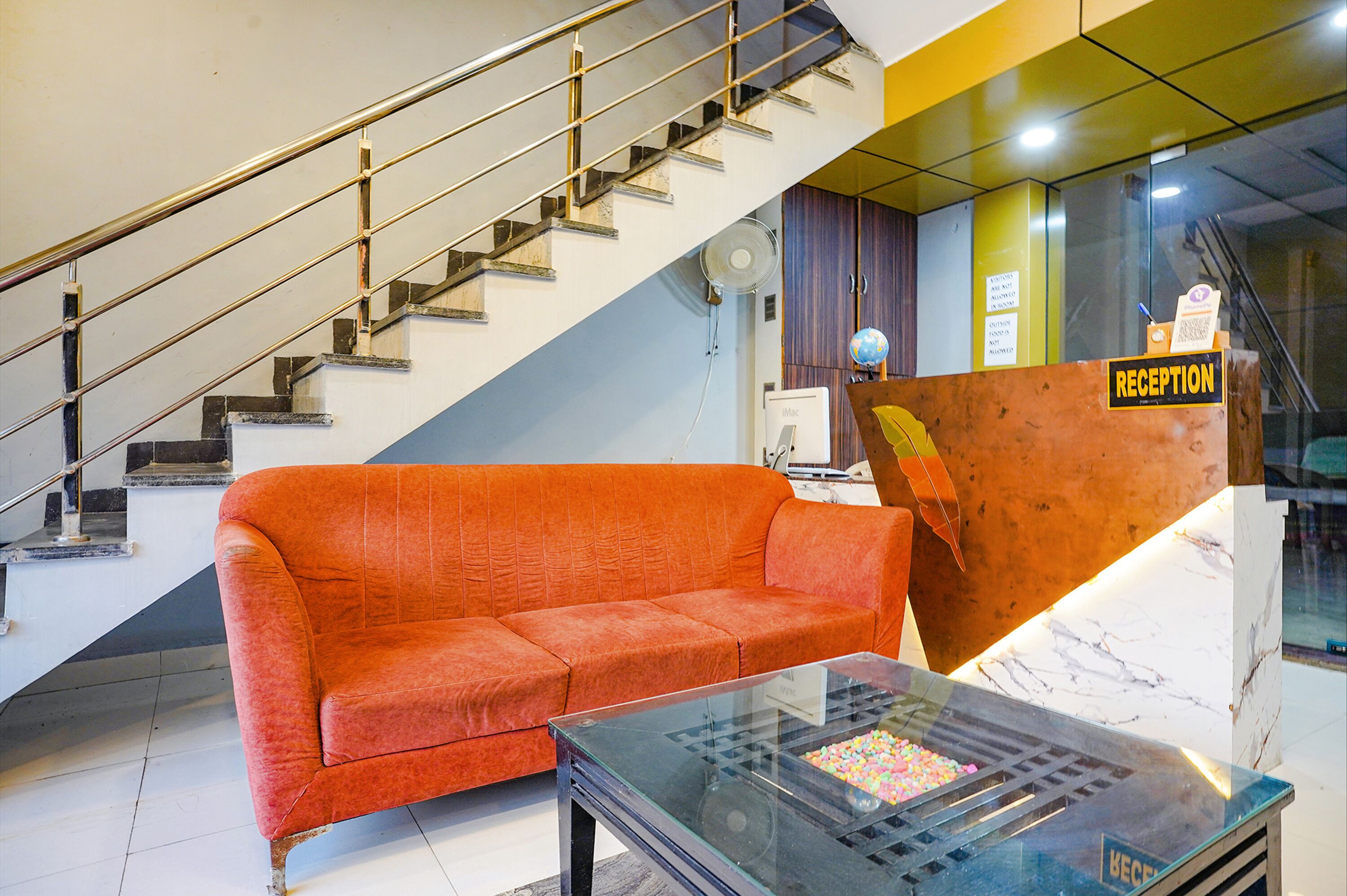 A reception area with a reception desk, a sofa, a glass coffee table, and a staircase.