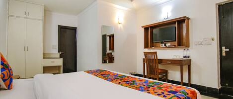 A hotel room with a bed, a desk, a chair, a wardrobe, and a television.