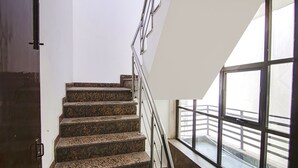 A staircase with a metal railing, a door on the left, and a large window on the right. - FabHotel JDM Residency (Gurugram)