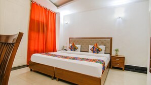 A neatly made bed with a colorful quilt, a wooden nightstand with a vase, and a chair. - FabHotel JDM Residency (Gurugram)