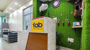 Una recepción de hotel con mostrador de mármol, pared verde con césped artificial, un reloj y un ventilador.