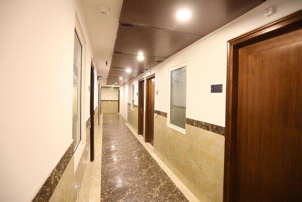 Un couloir d’hôtel avec un sol en marbre, des portes en bois et un mur recouvert de carreaux.