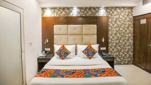 A hotel room with a large bed, a wooden headboard, a floral-patterned wall, and a nightstand with a phone and a lamp. - Fabhotel Station I (New Delhi)