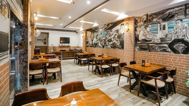 A restaurant with brick walls, wooden tables, and chairs. There is a mural on the wall depicting people in a dining setting. - Fabhotel Station I (New Delhi)