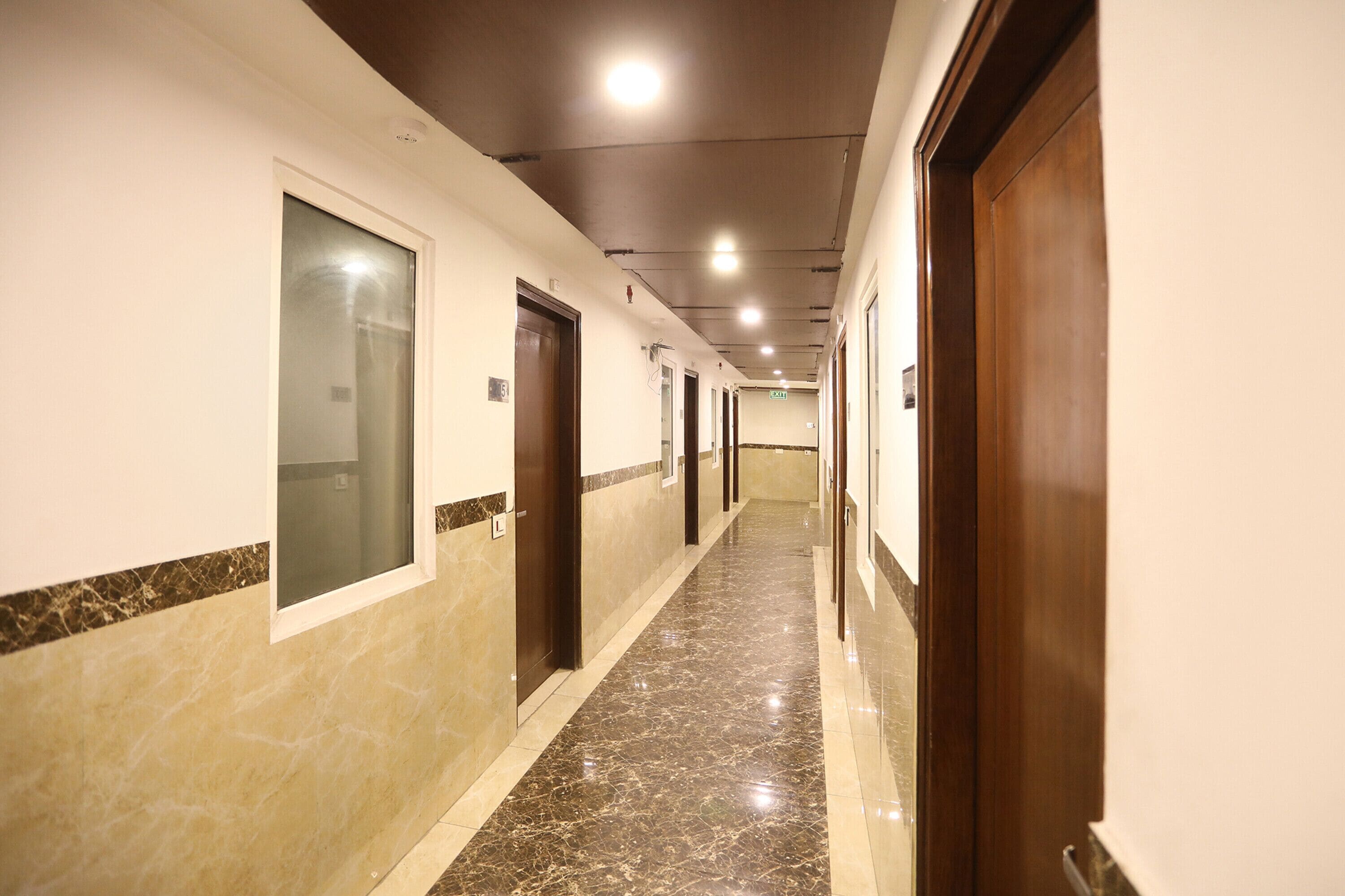 A long, narrow hotel corridor with marble flooring, wooden doors, and recessed lighting.