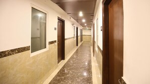 A long, narrow hotel corridor with marble flooring, wooden doors, and recessed lighting. - Fabhotel Station I (New Delhi)